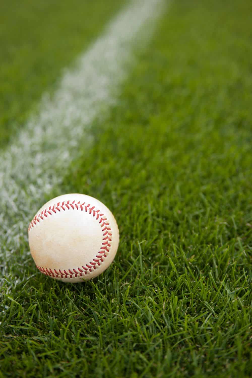 A baseball rests on green sports field artificial turf near a white chalk line on a field in Oahu, HI.