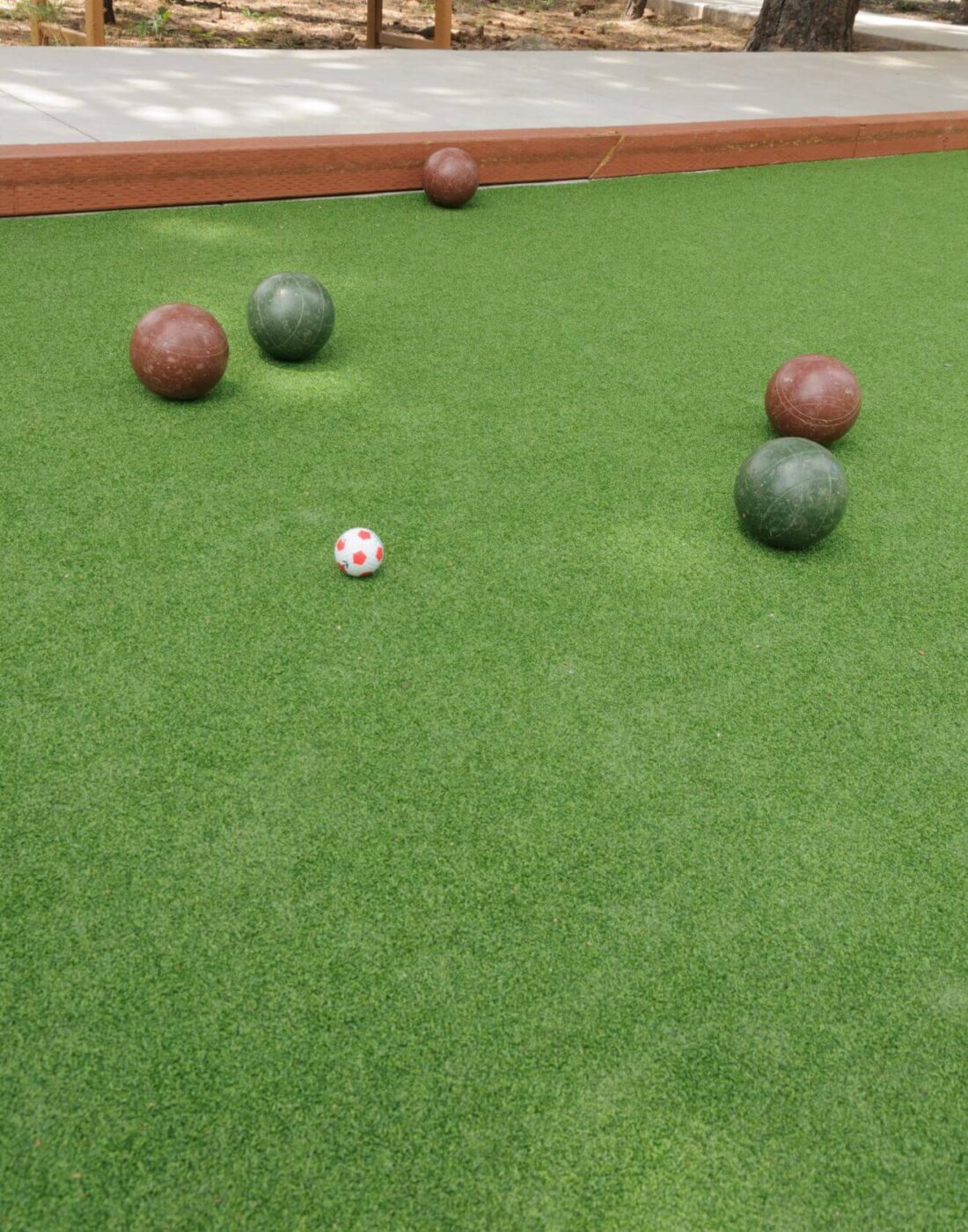 Several bocce balls, both green and brown, and a small white and red pallino ball are scattered on a sports field with artificial turf in Oahu, HI.